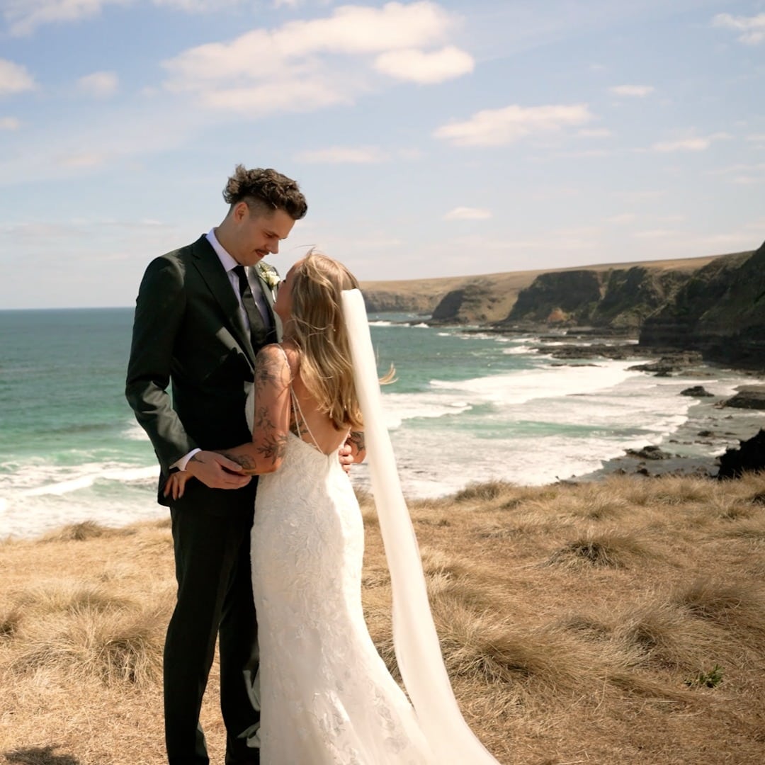 A bride and groom embracing on a clifftop above the ocean